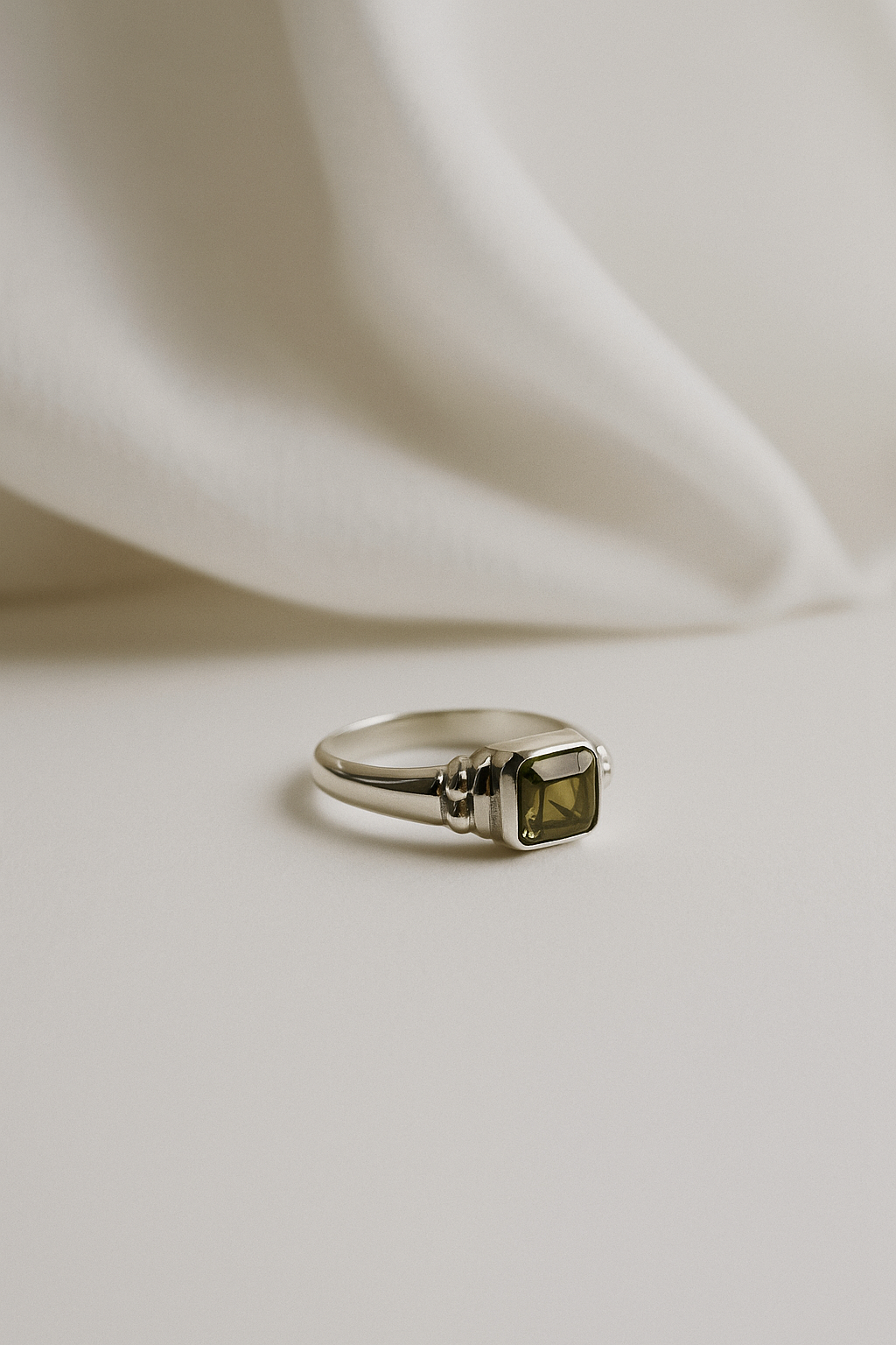 Silver ring with a green gemstone on a white fabric background